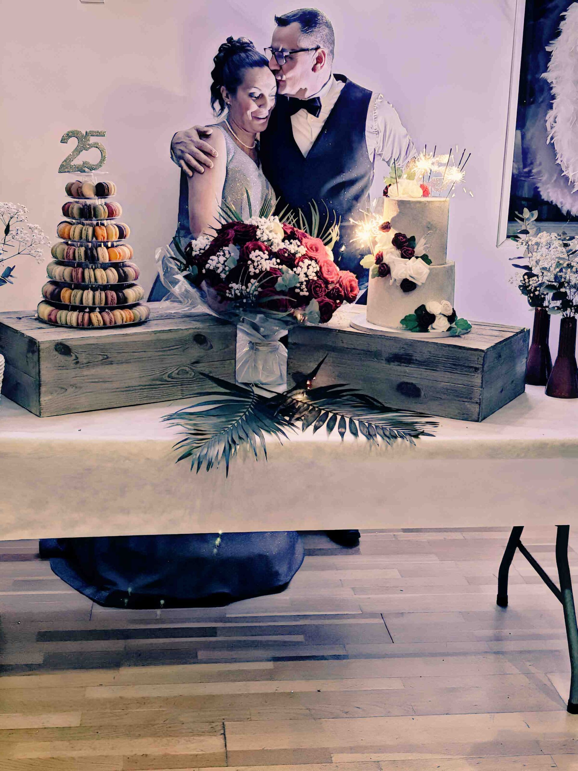 Martine et Didier Rémy embrassés devant leur gâteau d'anniversaire de mariage des 25 ans, entourés de macarons et de décorations festives